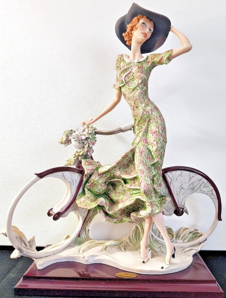 This figurine is a Giuseppe Armani sculpture titled "The Bicycle - Spring"