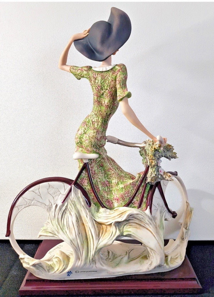 This figurine is a Giuseppe Armani sculpture titled "The Bicycle - Spring"